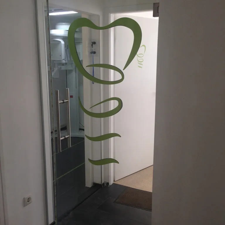 Eingang der Praxis mit Zahn-Logo auf der Glastür
